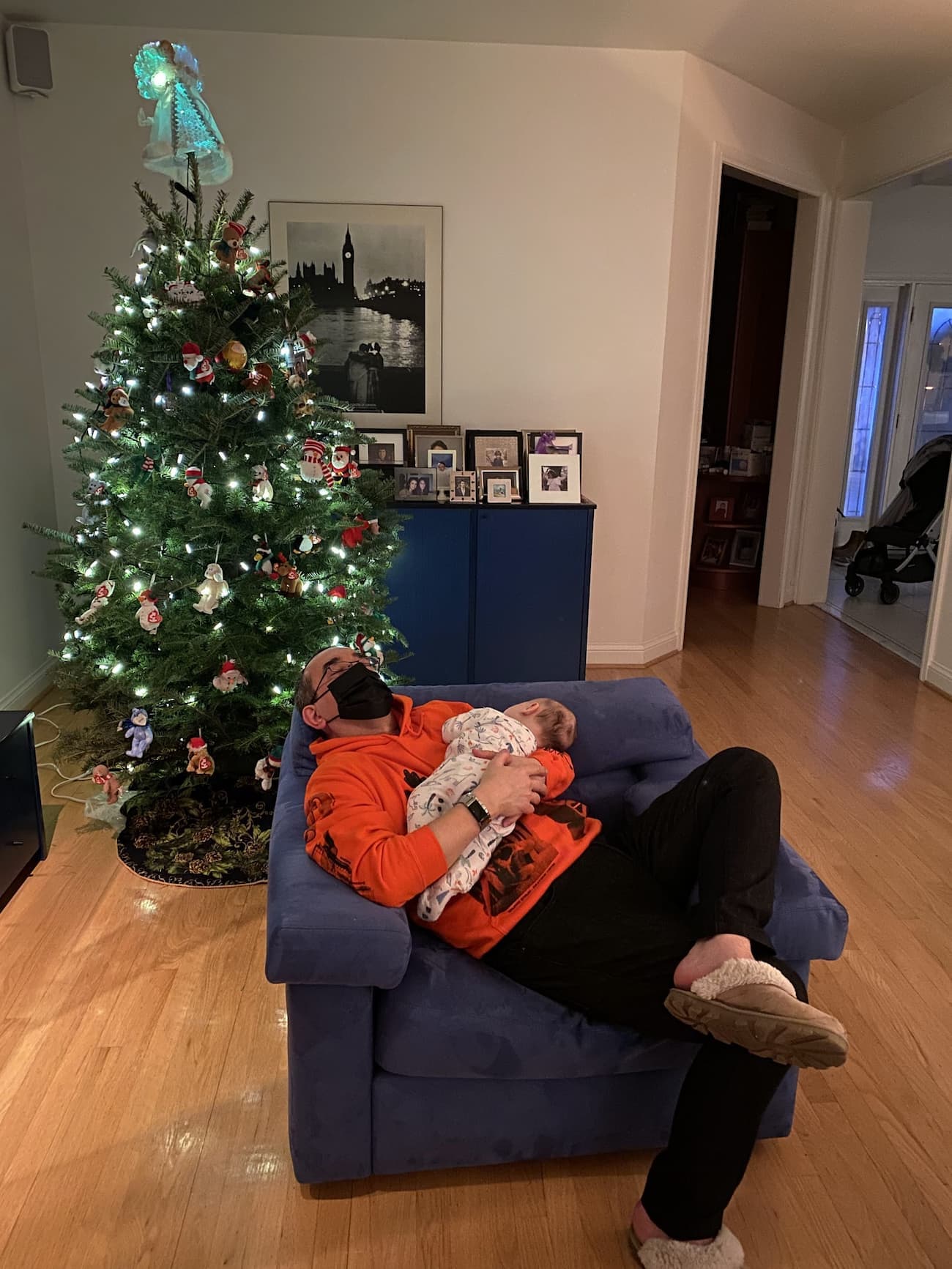 My dad, Santino, holding Baby O, both appearing to be asleep by a Christmas tree (though my dad is just pretending)